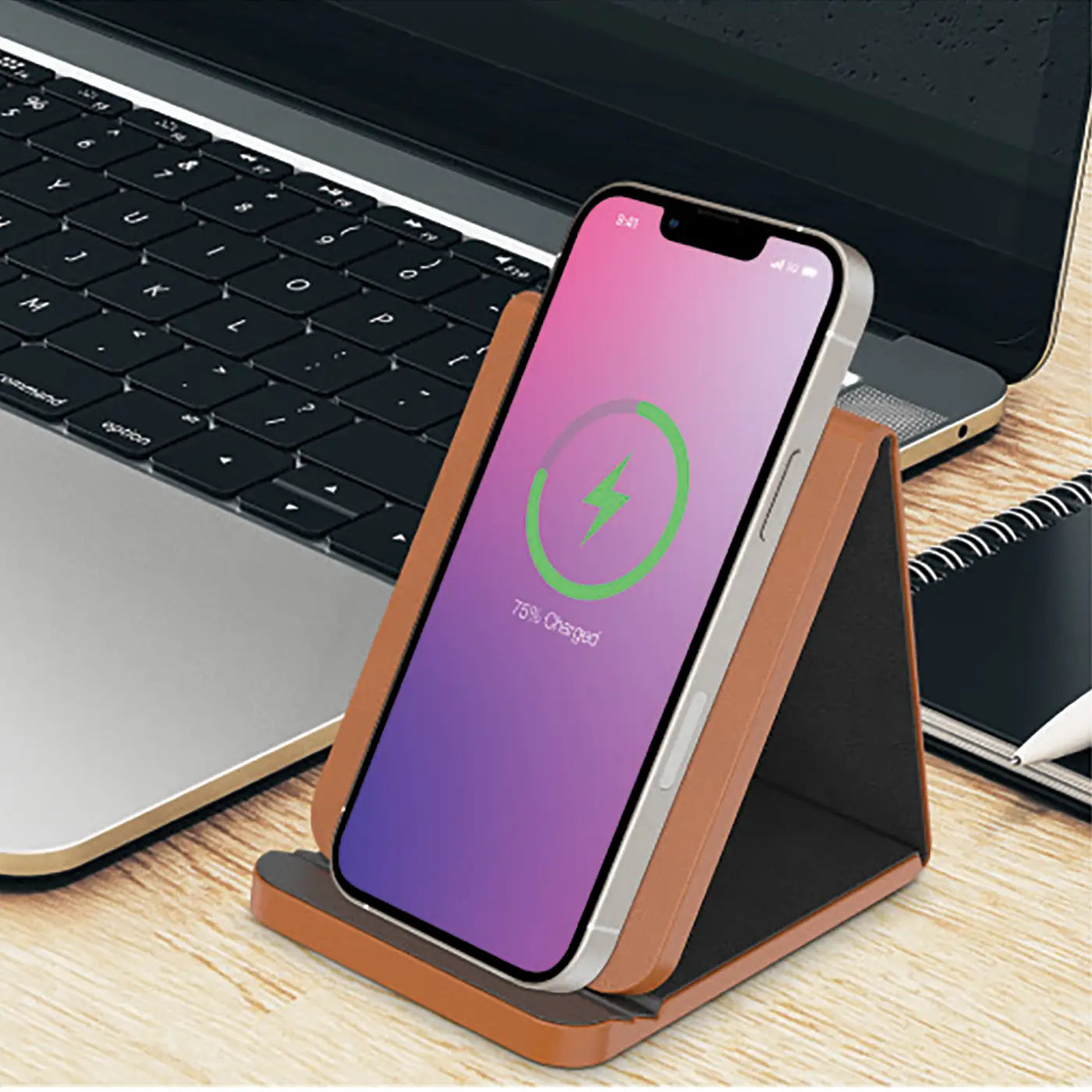 Smartphone on a stand with charging indicator next to a laptop on a desk