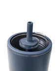Close-up of a matte slate blue insulated tumbler with a clear lid and matching blue straw insert, shown on a white background.
