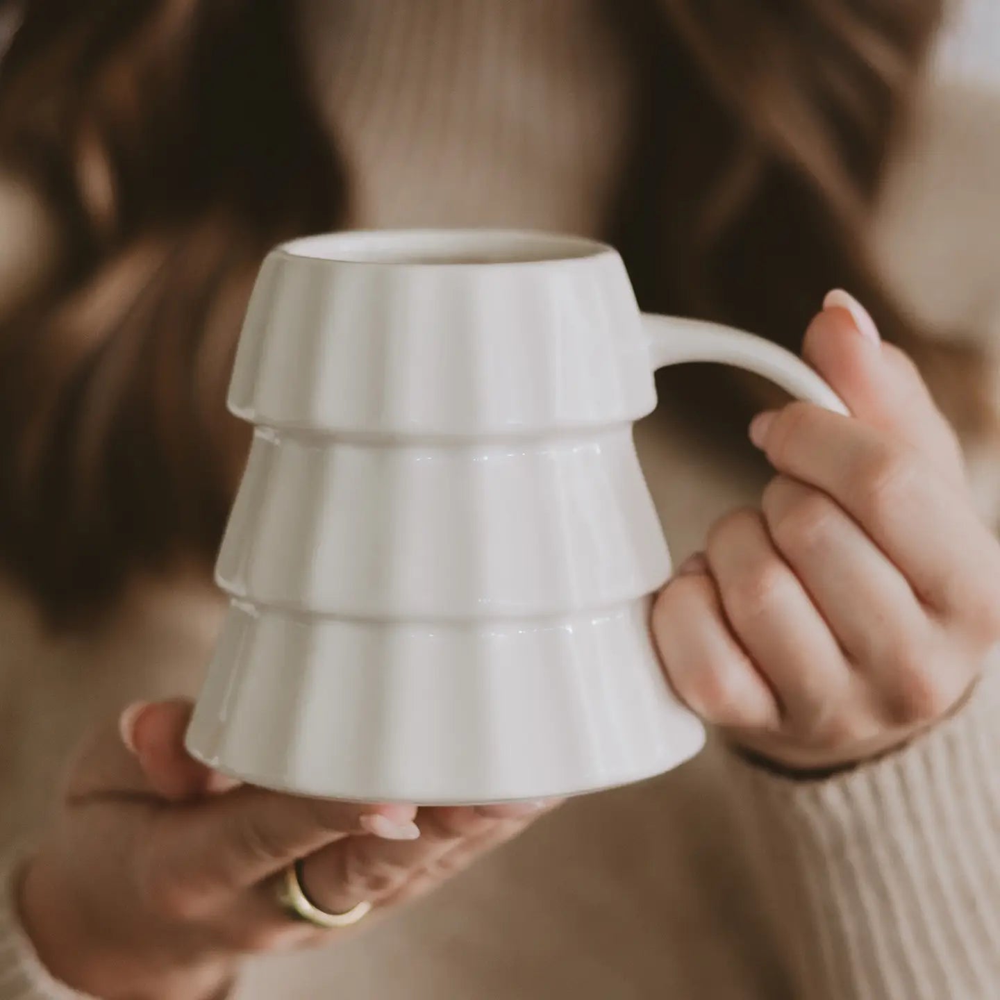 Person holding a white ceramic mug with a textured design.