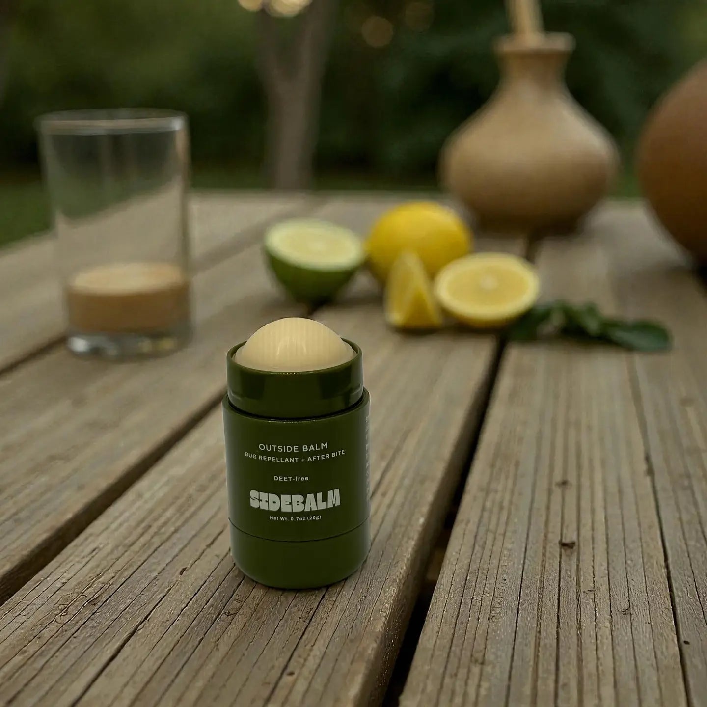 Green balm stick on a wooden surface with lemons and limes in the background