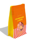 A stand-up pouch of sugarfina Champagne and Rosé candy, featuring a bright orange top half with yellow text, a yellow side panel, and pink-and-white diagonal stripes on the bottom, with a clear window showing the candy inside.