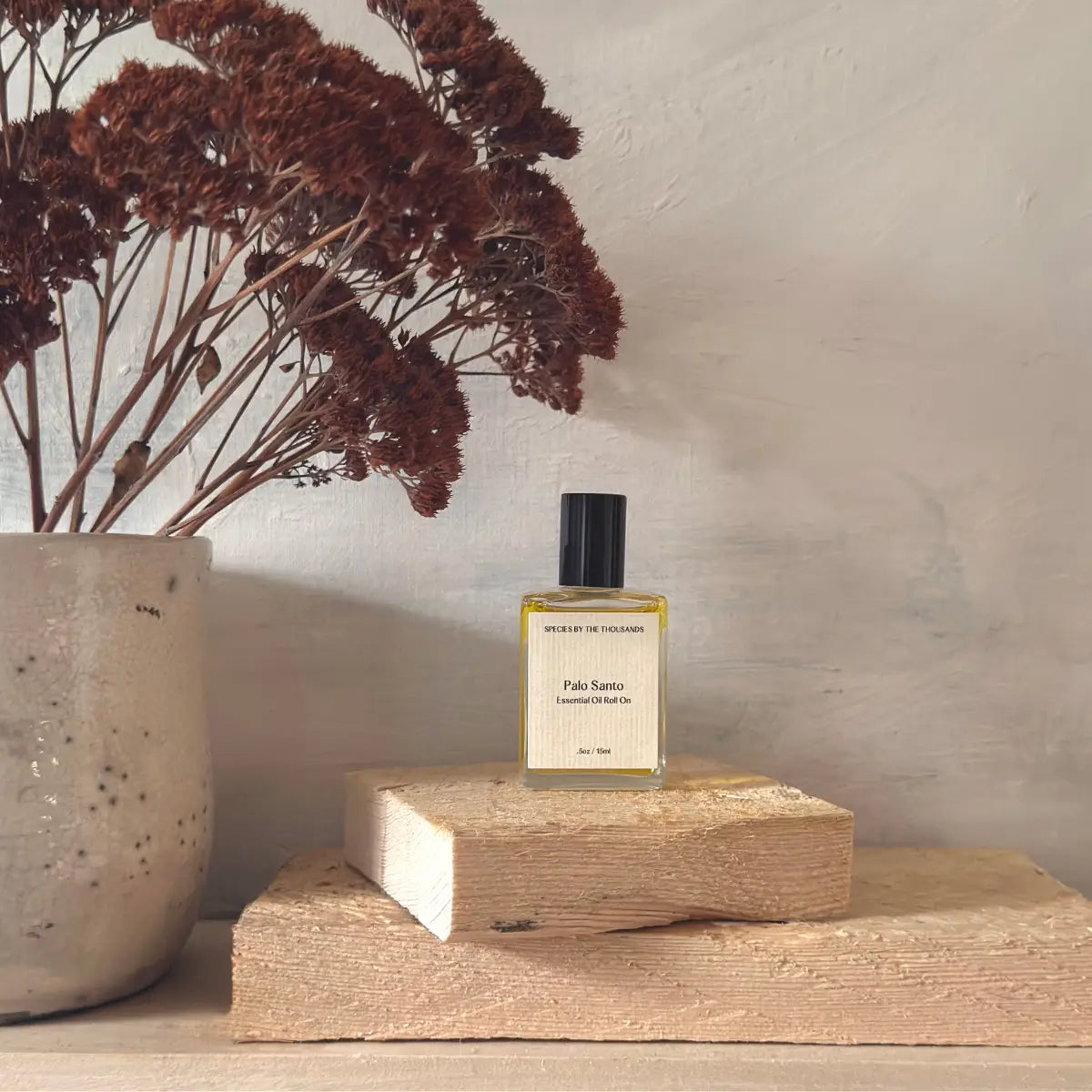 Perfume bottle on a wooden block with dried flowers in the background