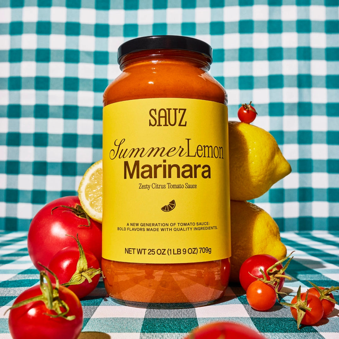 Jar of Sauz Summer Lemon Marinara sauce on a checkered tablecloth with lemons and tomatoes.