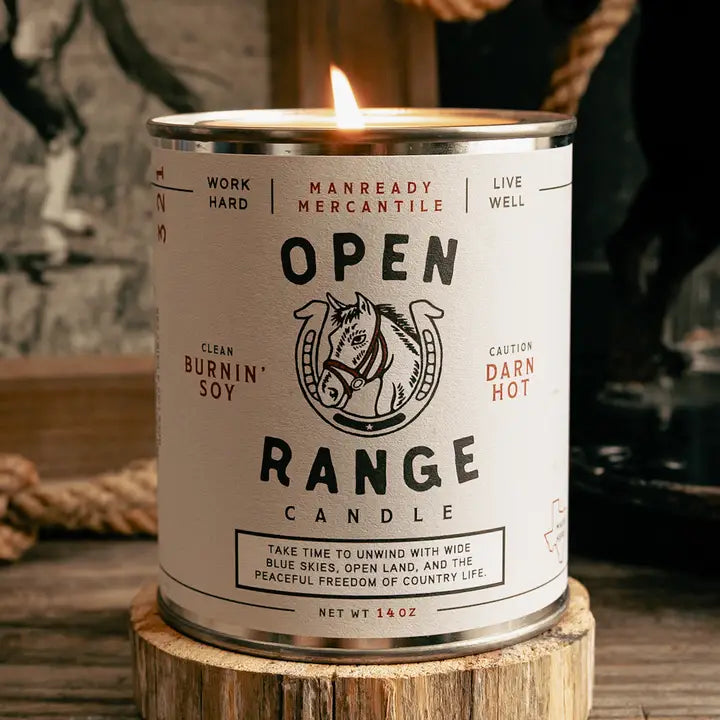 Candle in a can labeled 'Open Range' with branding on a wooden surface.