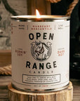 Candle in a can labeled 'Open Range' with branding on a wooden surface.