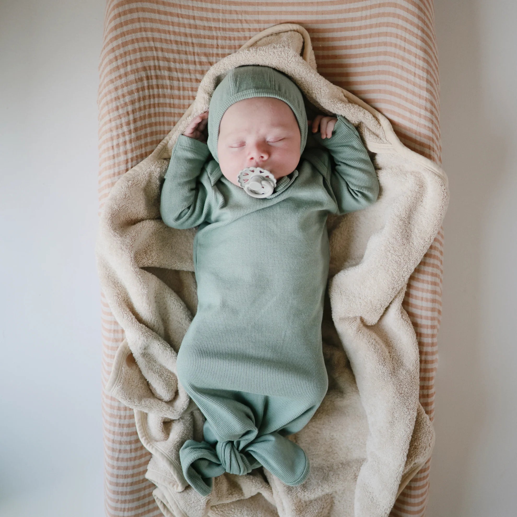 baby in green Mushie baby gown