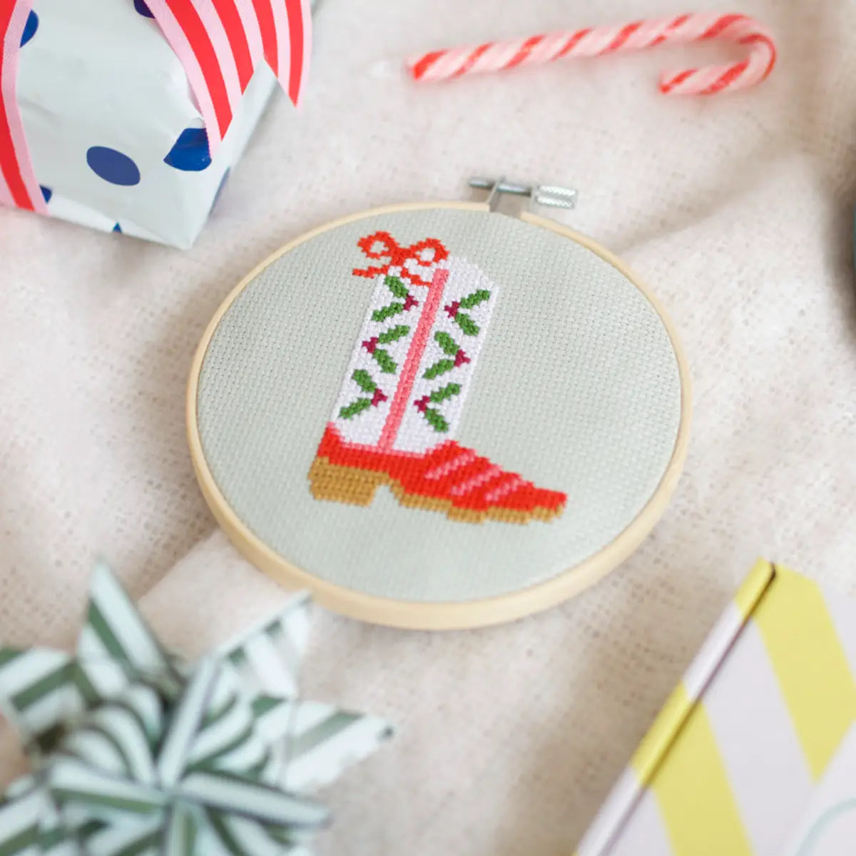 Embroidery hoop with a red boot and holly design on a beige fabric background.