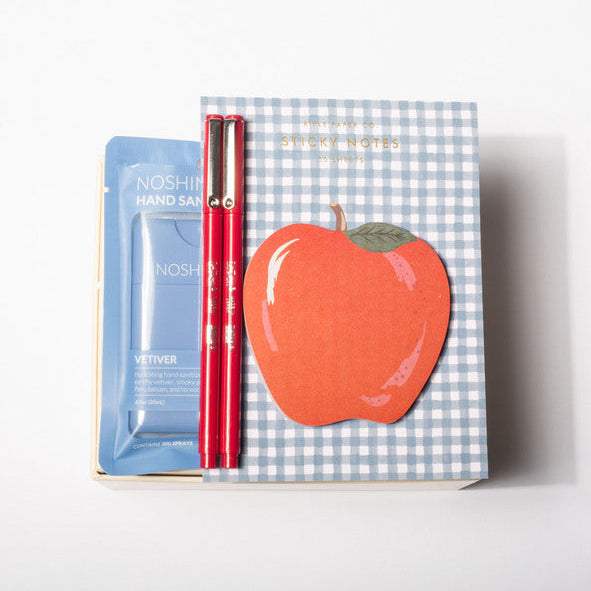 A boxed set containing a blue packet of NARS Hand Sanitizer, a red pen, and a decorative box with a blue gingham pattern and a large red apple illustration, photographed on a clean white background.