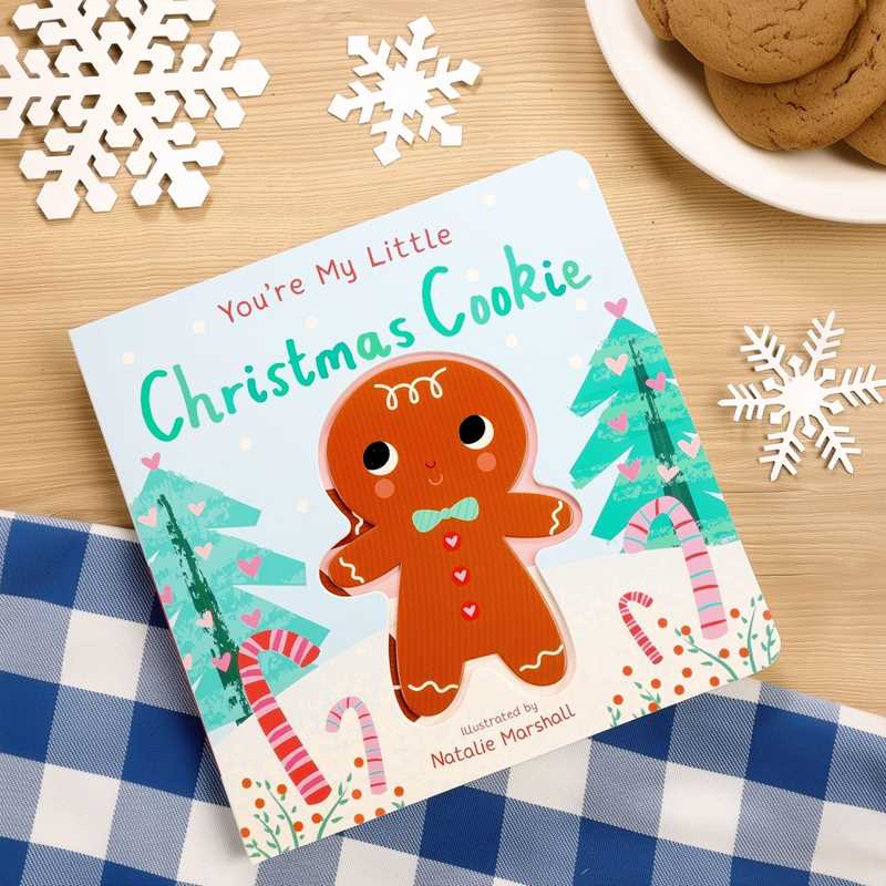 Children's book titled 'You're My Little Christmas Cookie' with a gingerbread man illustration on a wooden table with cookies and snowflakes.