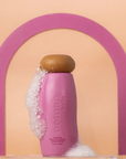 Pink bottle with wooden cap on a peach background with a pink arch