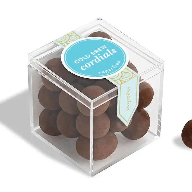 Clear cube box with brown round candies and a blue label on a white background