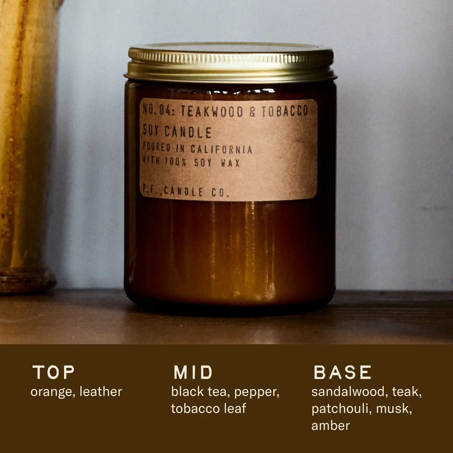 Brown candle with a label on a wooden surface, featuring a description of its fragrance profile.