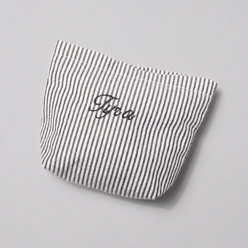 A small fabric pouch with thin black and white vertical stripes and the name 'Fyra' embroidered in black script on the front, photographed on a light gray background.