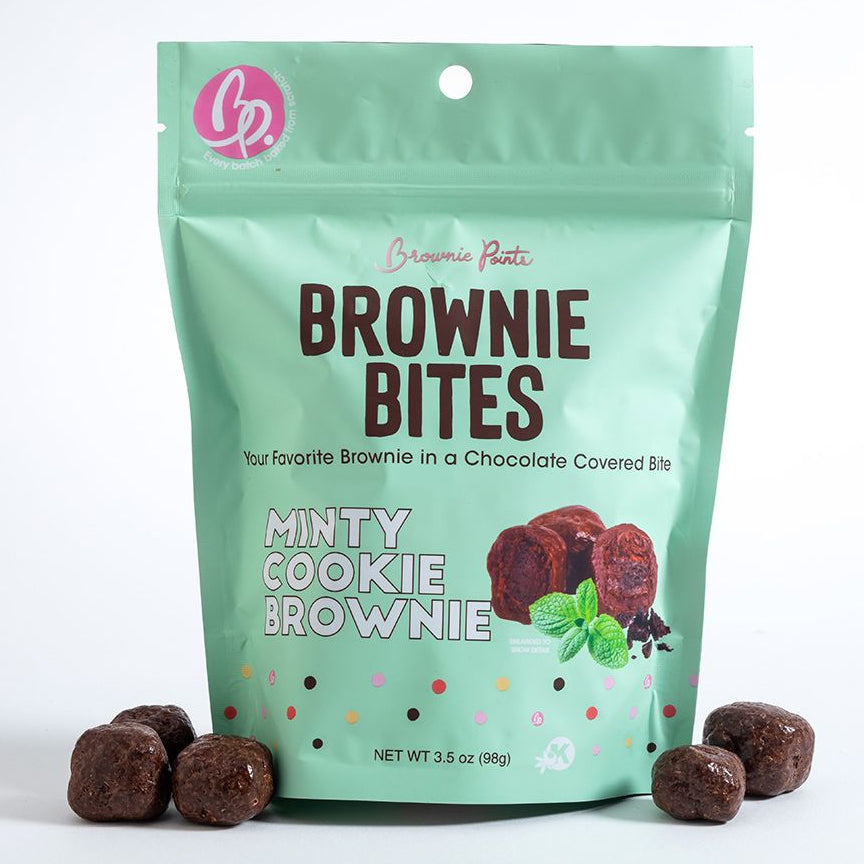 Green package of Minty Cookie Brownie Bites with brownies and mint leaves on a white background