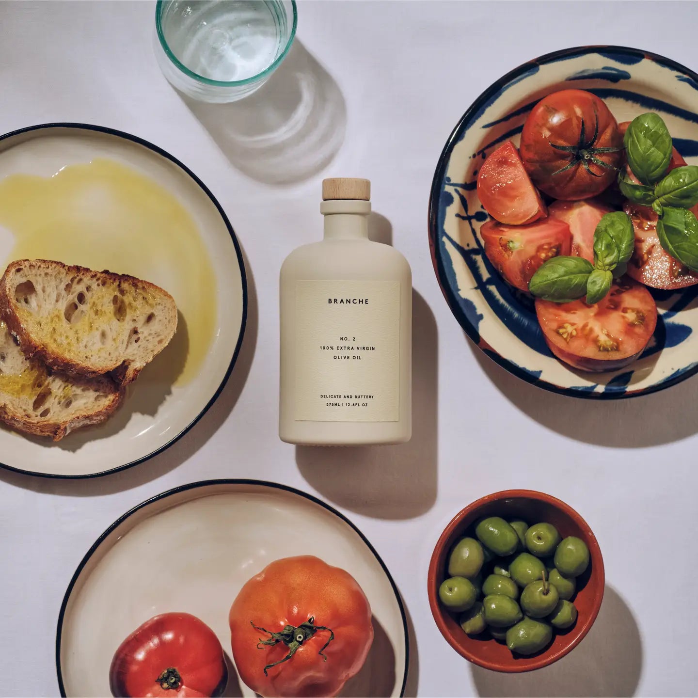 Branche olive oil bottle with bread, tomatoes, and olives on a table
