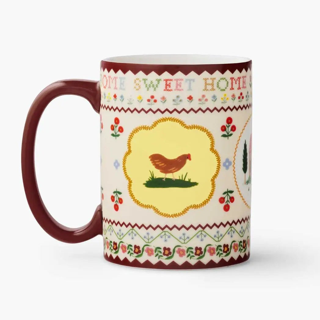 A ceramic mug with a dark red handle and interior, decorated with a cream-colored patterned band featuring a central yellow shield with a brown chicken and the words 'DON'T SWEET HOME'.