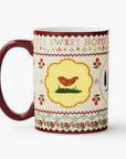 A ceramic mug with a dark red handle and interior, decorated with a cream-colored patterned band featuring a central yellow shield with a brown chicken and the words 'DON'T SWEET HOME'.