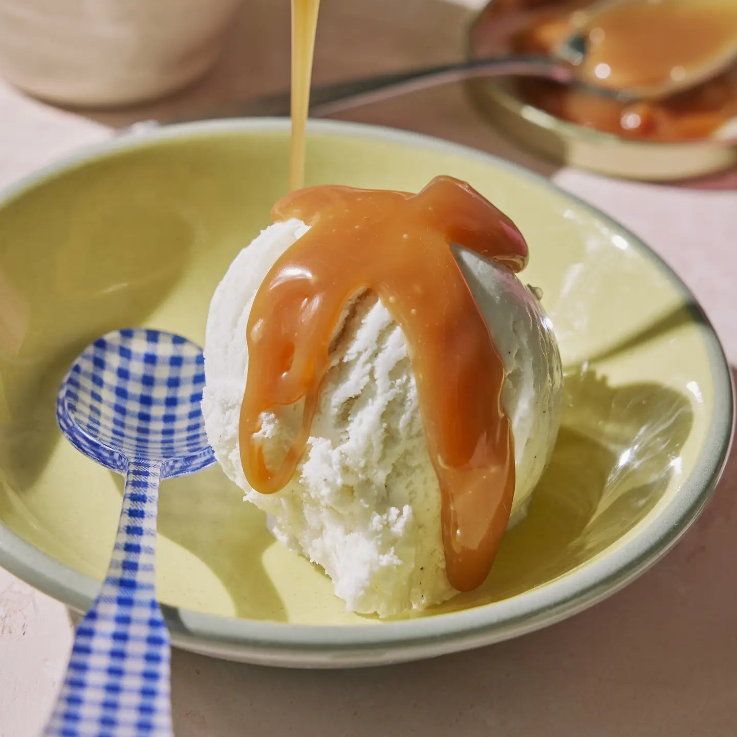Ice cream with caramel sauce being poured onto a yellow plate