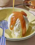Ice cream with caramel sauce being poured onto a yellow plate