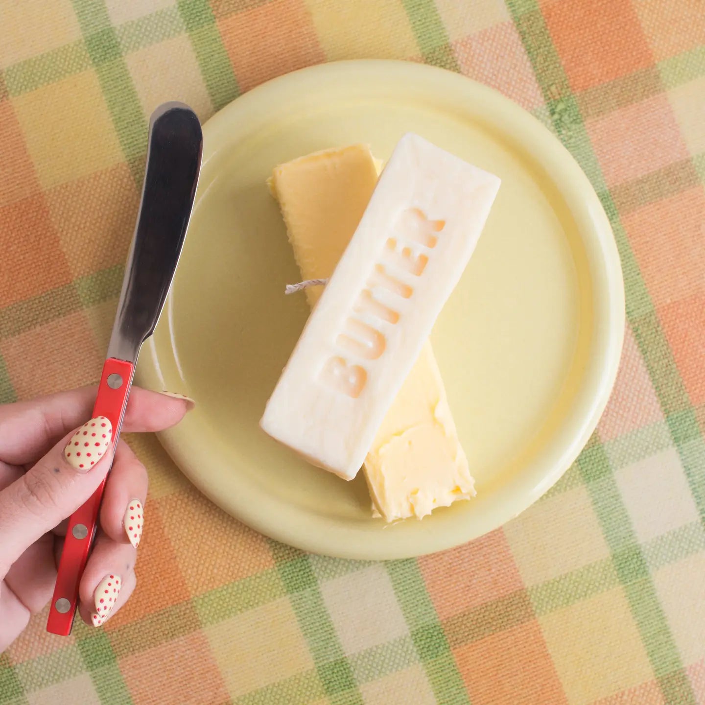 Butter block with a knife on a yellow plate on a checkered tablecloth