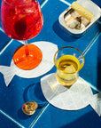 Two glasses of red and yellow drinks on fish-shaped coasters with a blue tiled background.