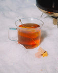 Clear mug of hot tea with a teabag on a snowy surface
