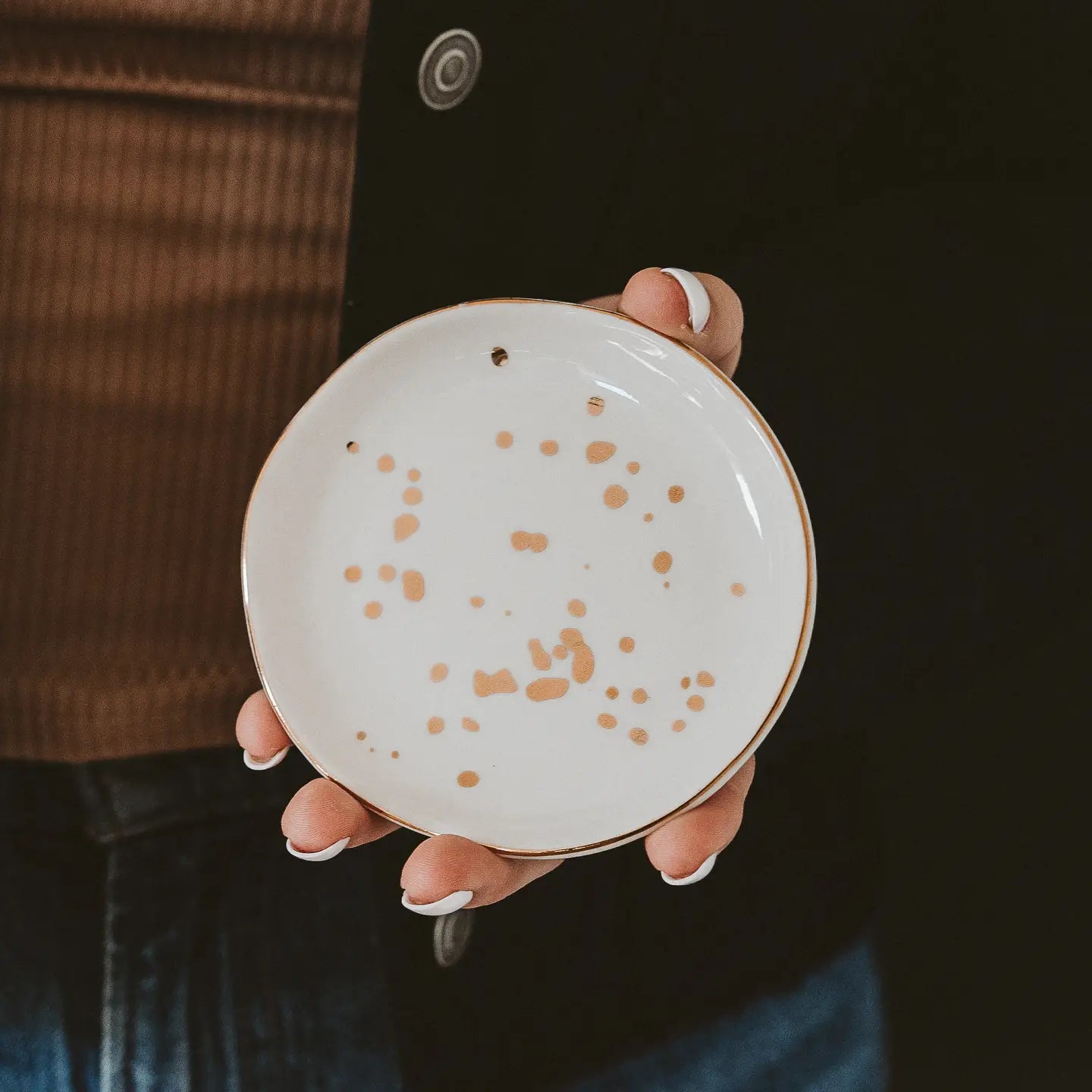 Person holding a ceramic plate with brown speckles against a dark background