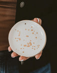 Person holding a ceramic plate with brown speckles against a dark background