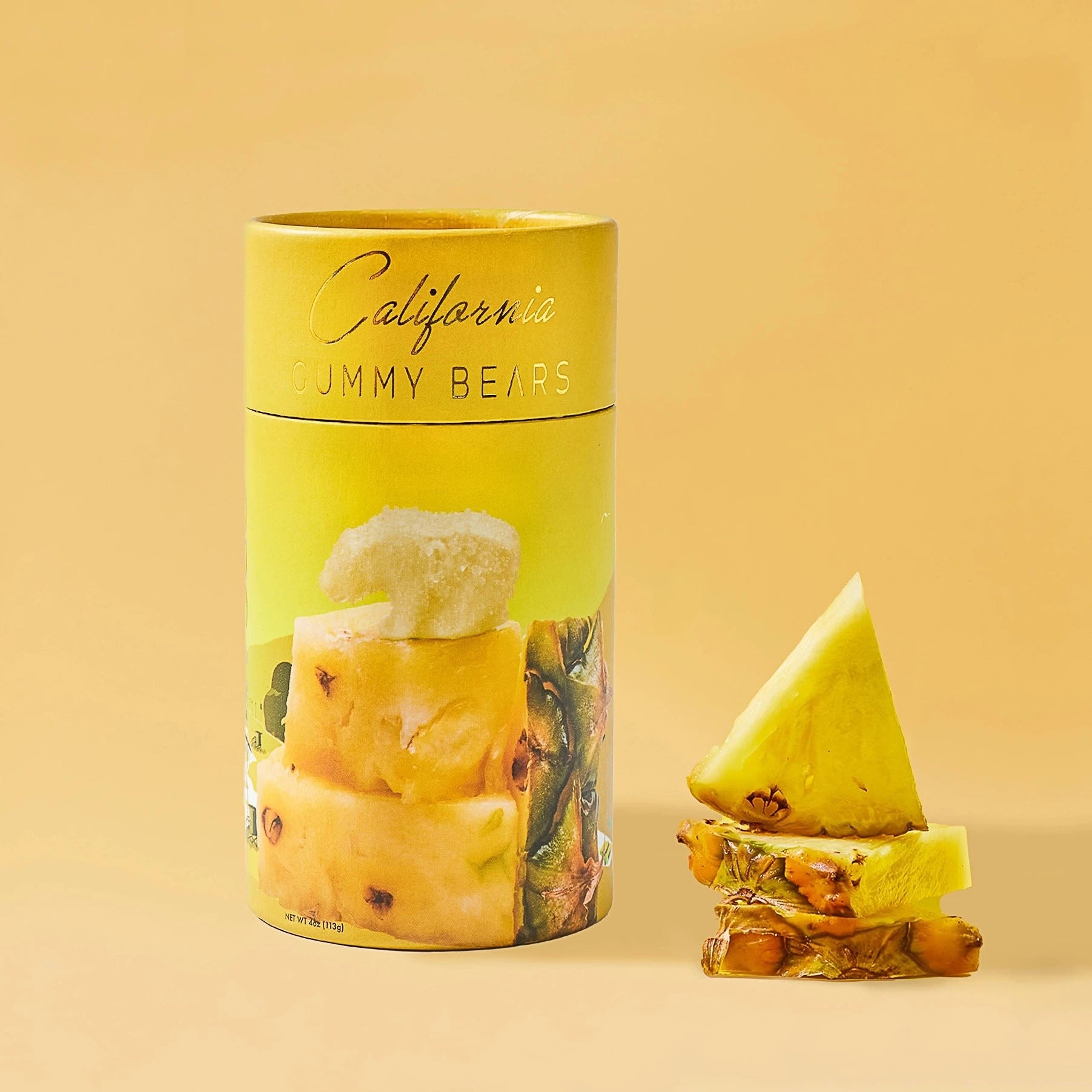 yellow cylinder with gold text on the top. has picture of bear gummy sitting on top of pineapple