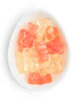 Gummy bear candies in translucent orange, pink, and pale yellow colors, arranged inside a white oval dish on a white background.