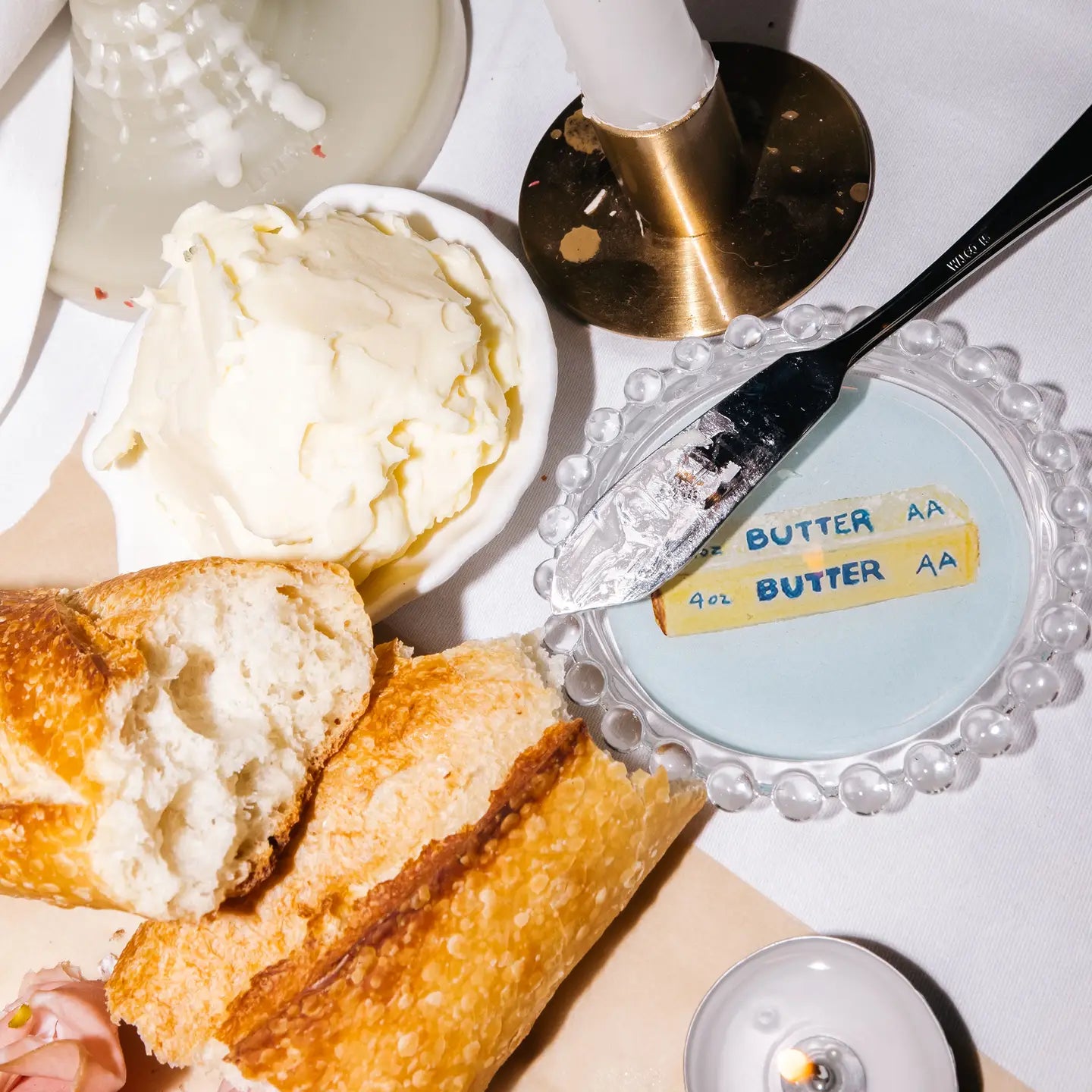 Butter dish with a stick of butter, bread, and a knife on a white surface.