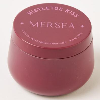 A small, round, maroon-colored candle tin with a matte finish, labeled "Mistletoe Kiss" and "MERSEA." The label also shows the weight as 3.5 oz and indicates it is a scented candle.