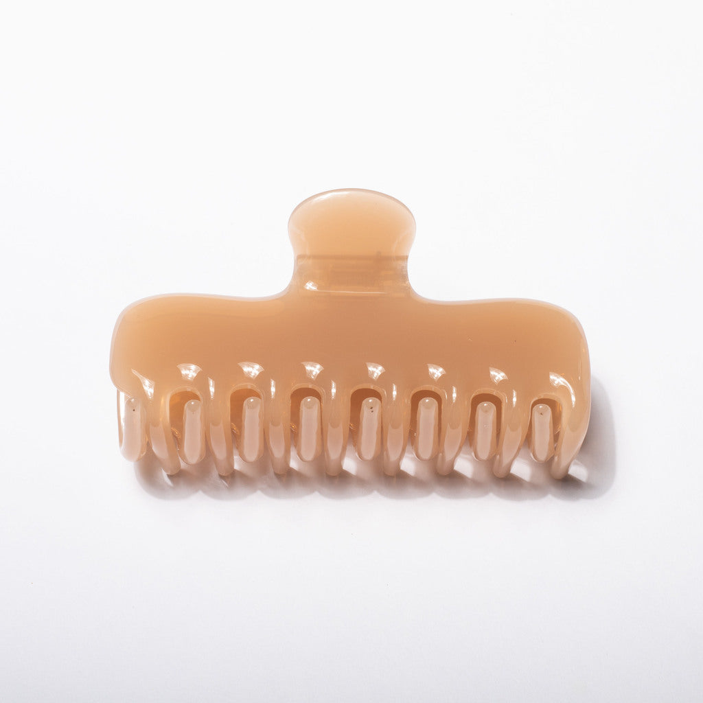 A single wide-tooth hair claw clip in a glossy, warm peach-beige translucent plastic, shown on a clean white background.