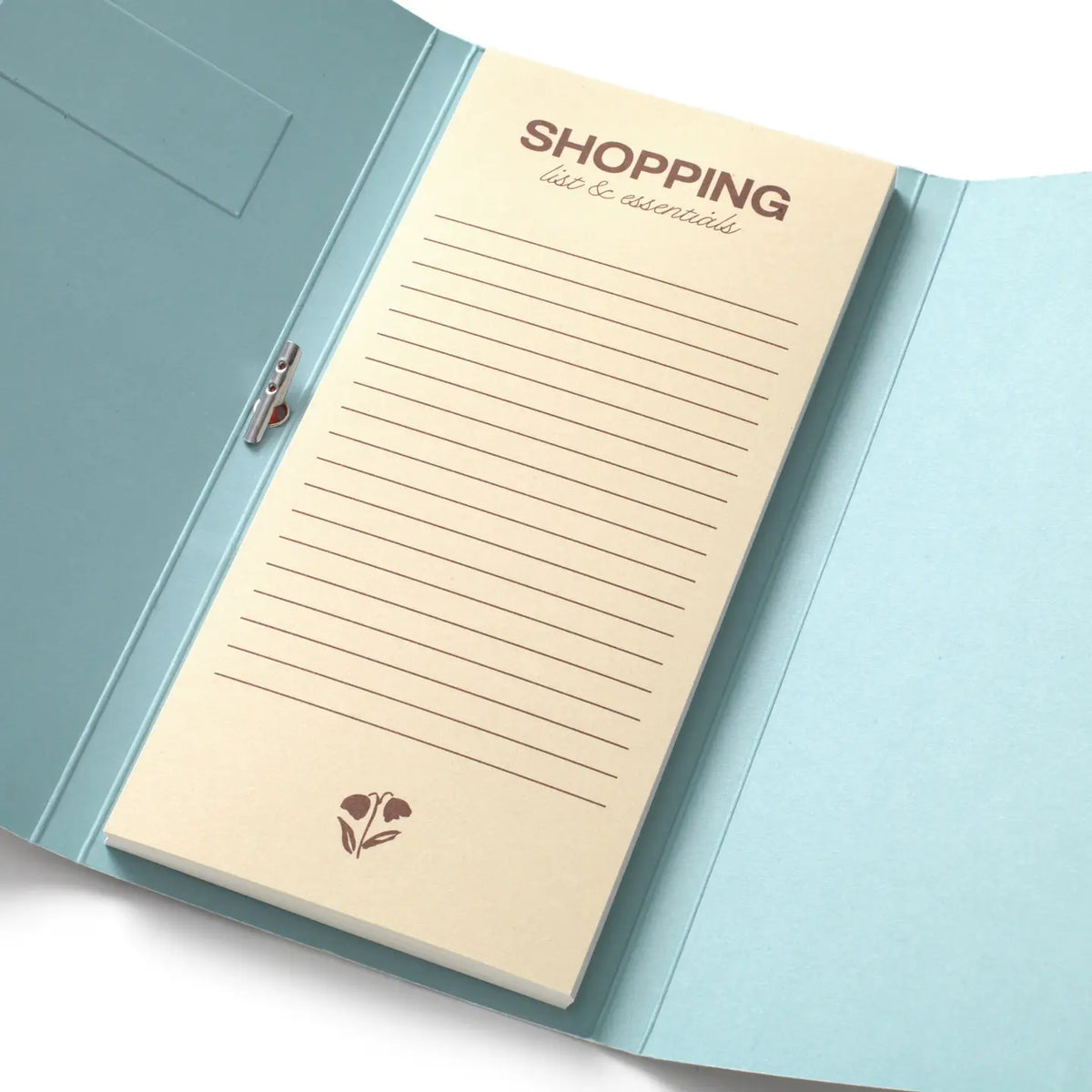 A light blue notebook with a cream-colored lined notepad insert that reads 'SHOPPING list & essentials,' photographed on a clean white background.