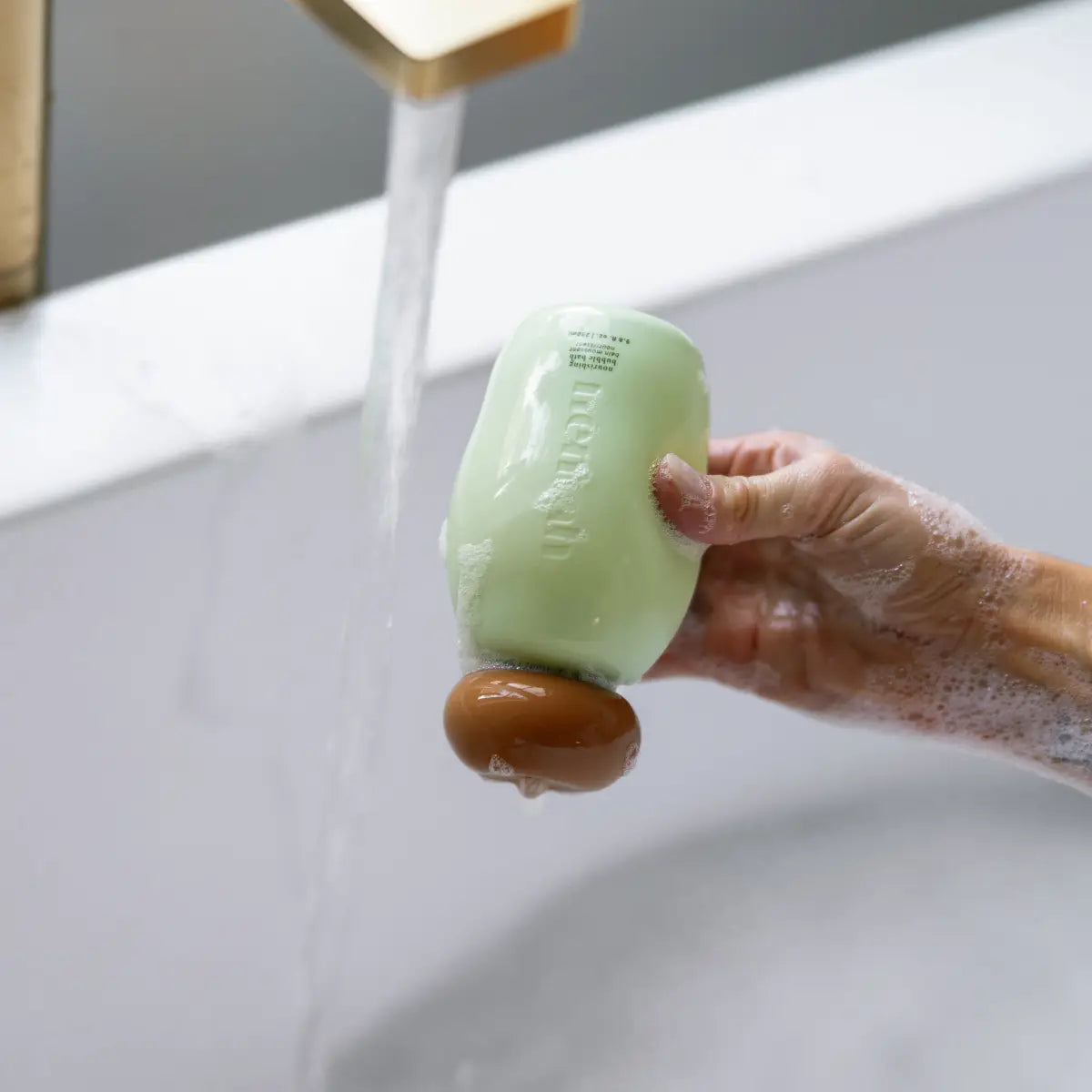 Hand holding a bar of soap under running water in a sink
