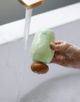Hand holding a bar of soap under running water in a sink