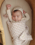 Baby sleeping in a moses basket with a checkered blanket and star-patterned hat.