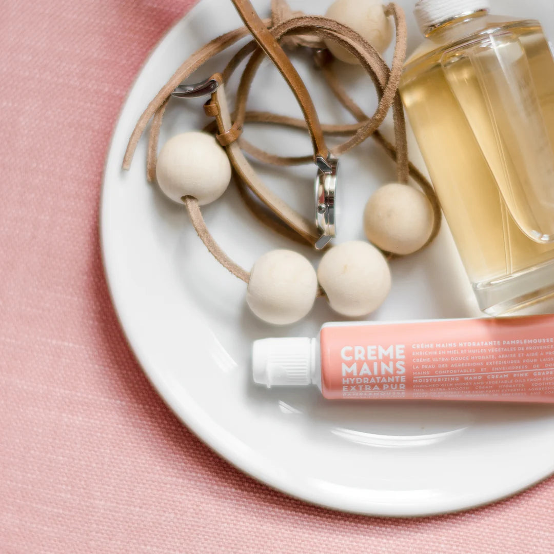 Hand cream, necklace, and bottle on a white plate with pink background