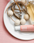 Hand cream, necklace, and bottle on a white plate with pink background