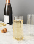 Faceted Crystal Stemless Champagne Flutes filled with champagne, with champagne bottle, cork and bottle opener in the background