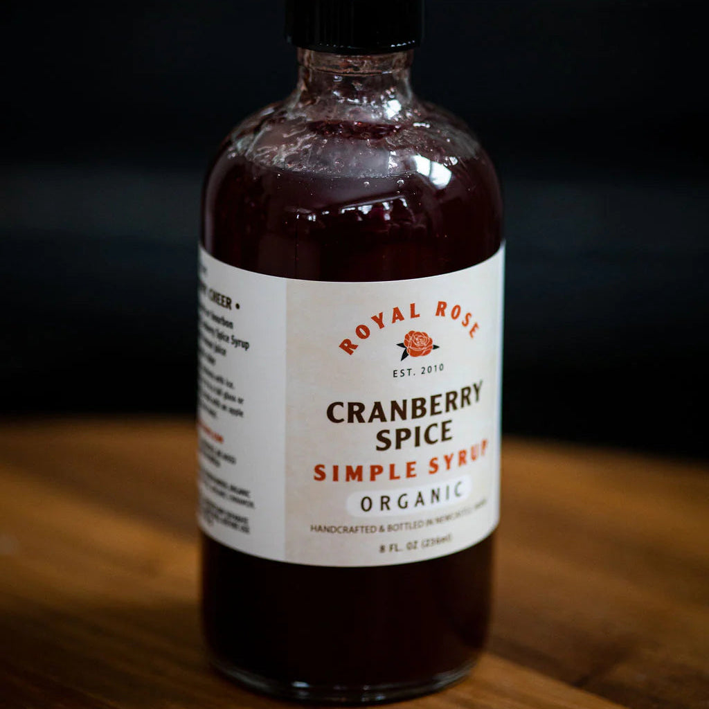 Bottle of Royal Rose Cranberry Spice Simple Syrup on a wooden surface with a blurred background