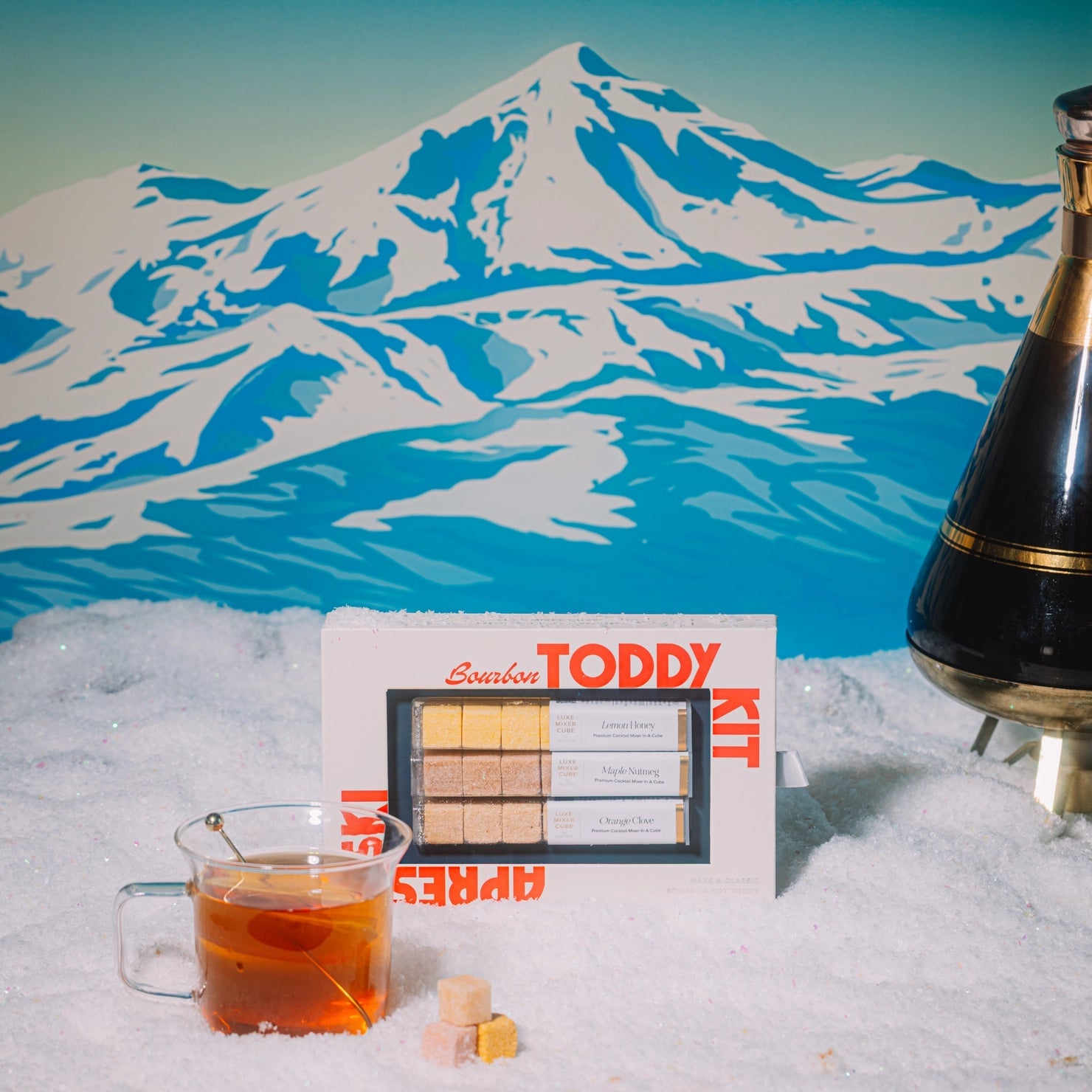 Toddy Kit with a glass of liquid in front of a mountainous landscape