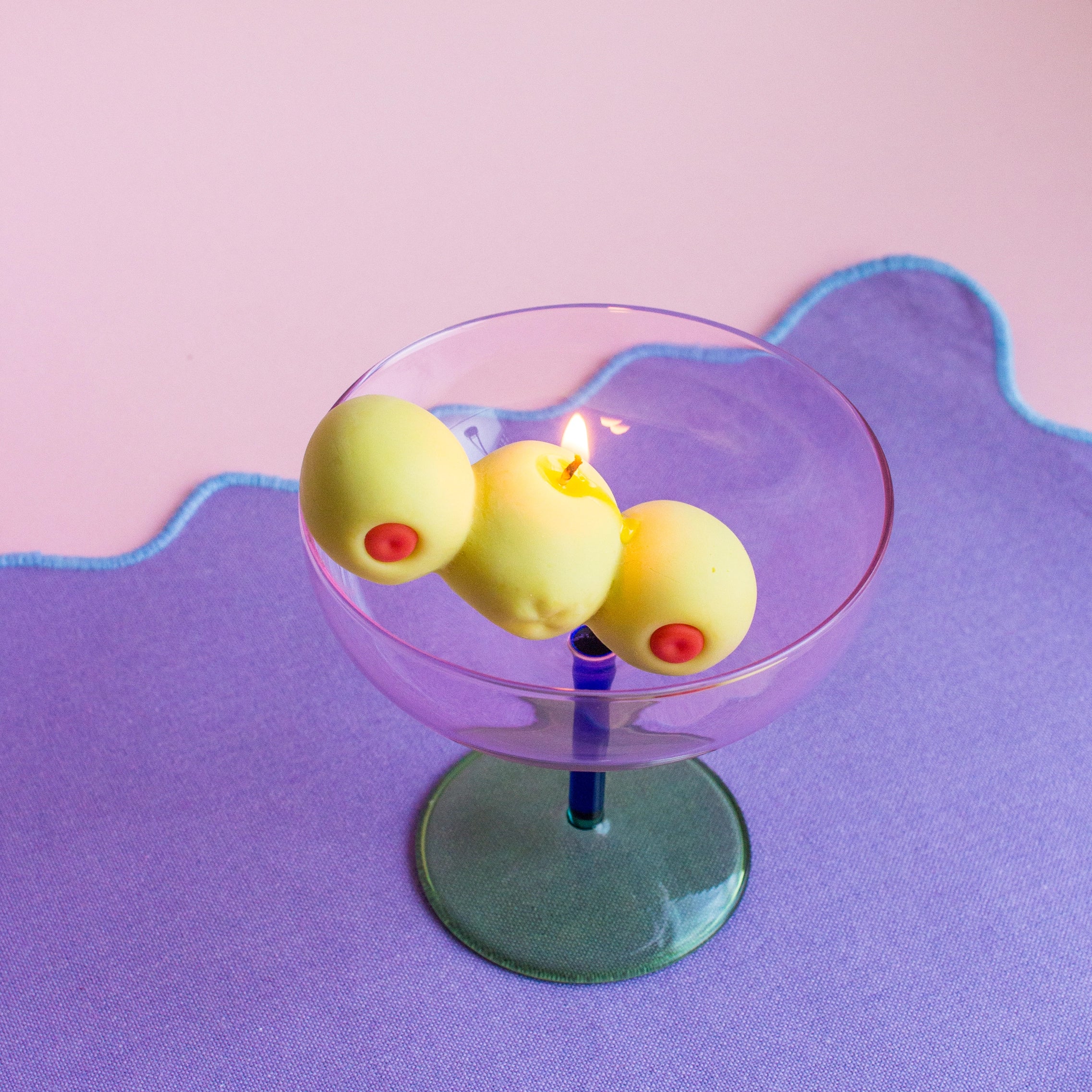 Candle in a glass holder with three yellow candles on a purple surface