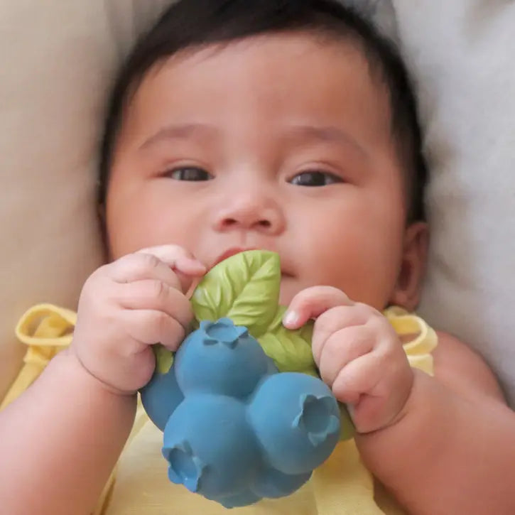 Baby holding a blueberry-shaped teething toy with green leaves