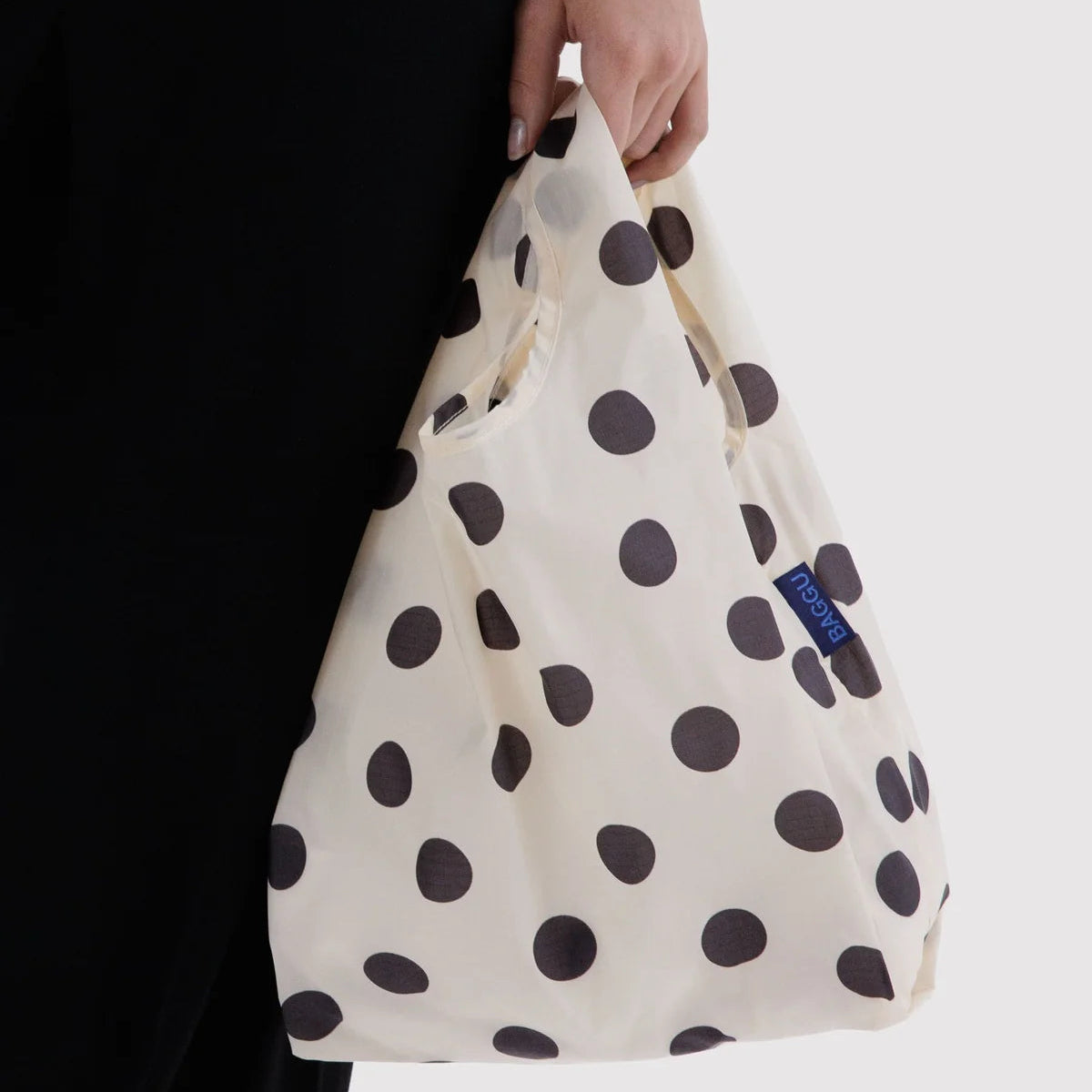 Person holding a white bag with black polka dots, featuring a visible brand logo.