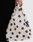 Person holding a white bag with black polka dots, featuring a visible brand logo.