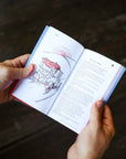 Person holding an open book with illustrations and text on a dark wooden surface