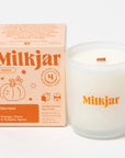 clear glass candle with "MILKJAR" printed on it in orange next to packaging box 