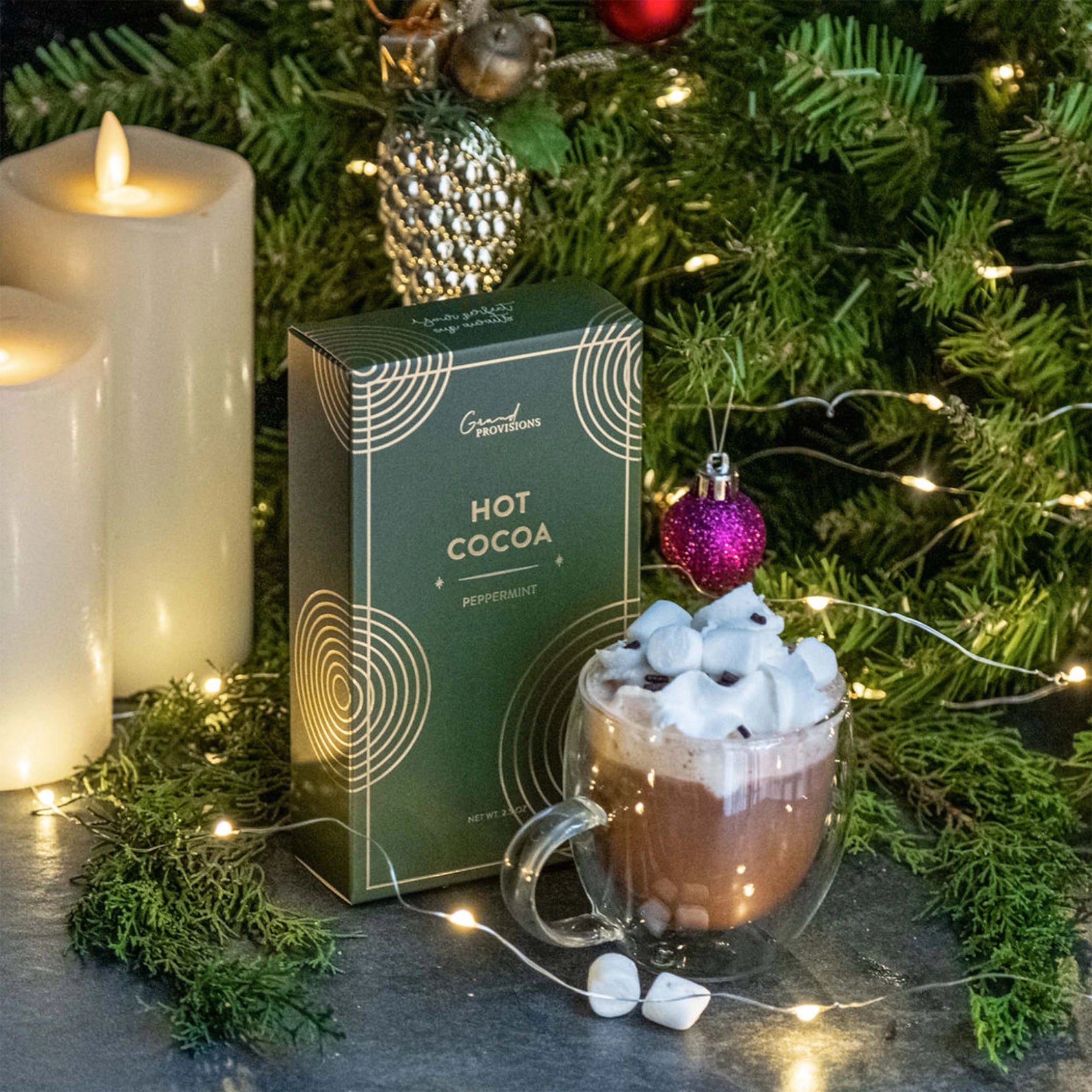 Hot chocolate with marshmallows, a box of Grand Marnier hot cocoa, and Christmas decorations on a table.
