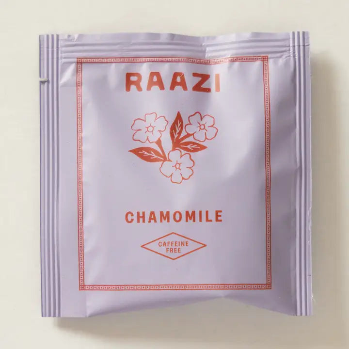 A single packet of RAAZI Chamomile caffeine-free tea, featuring a light lavender-white packaging with a coral-red floral design and text, set against a solid light beige background.